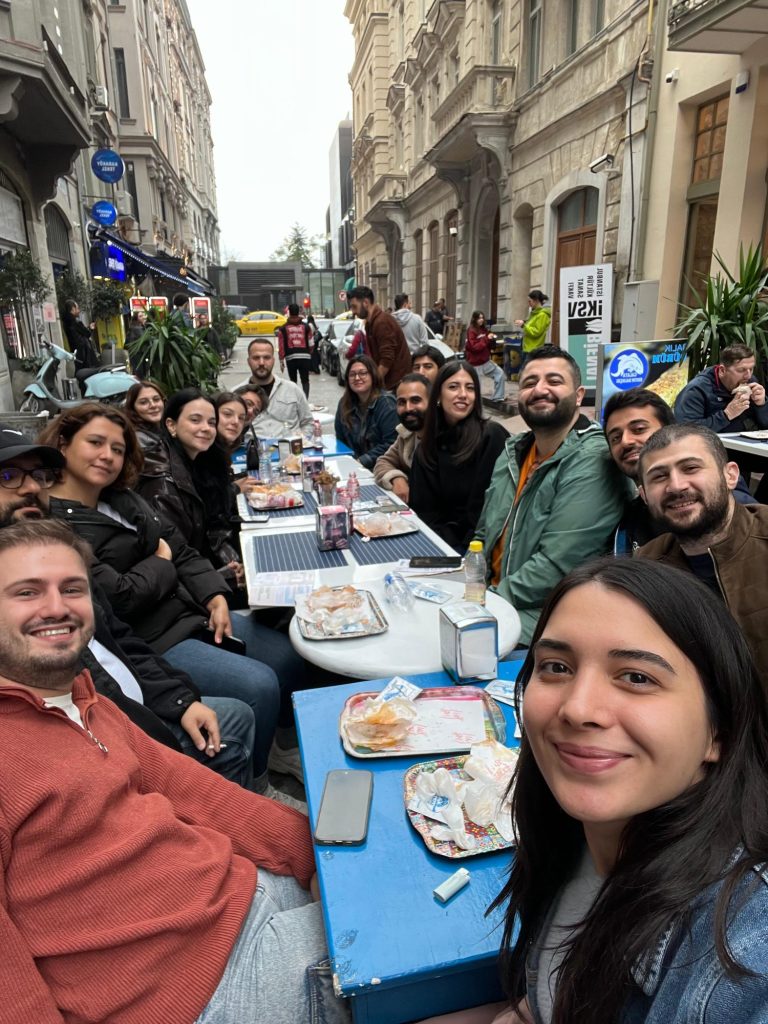 Tarihi binalar arasındaki dar sokakta uzun masada oturan kalabalık grup