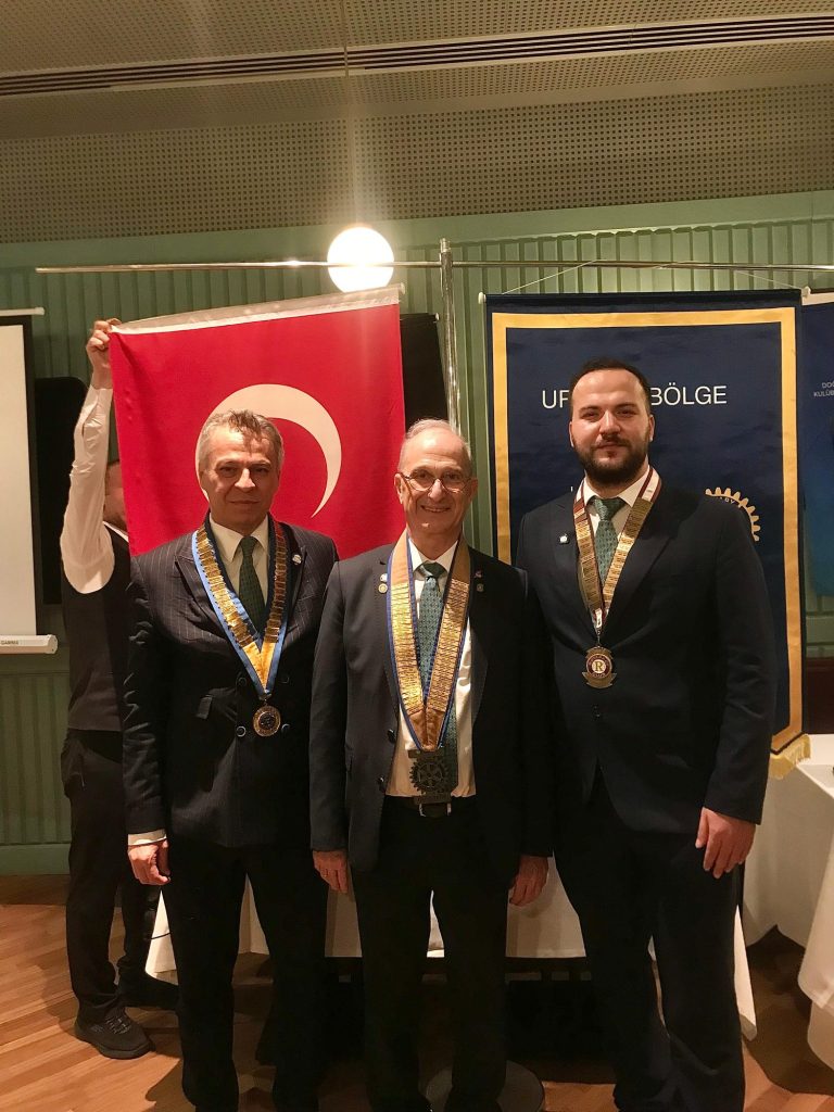 Bayrak önünde yakalıklı üç Rotary üyesi