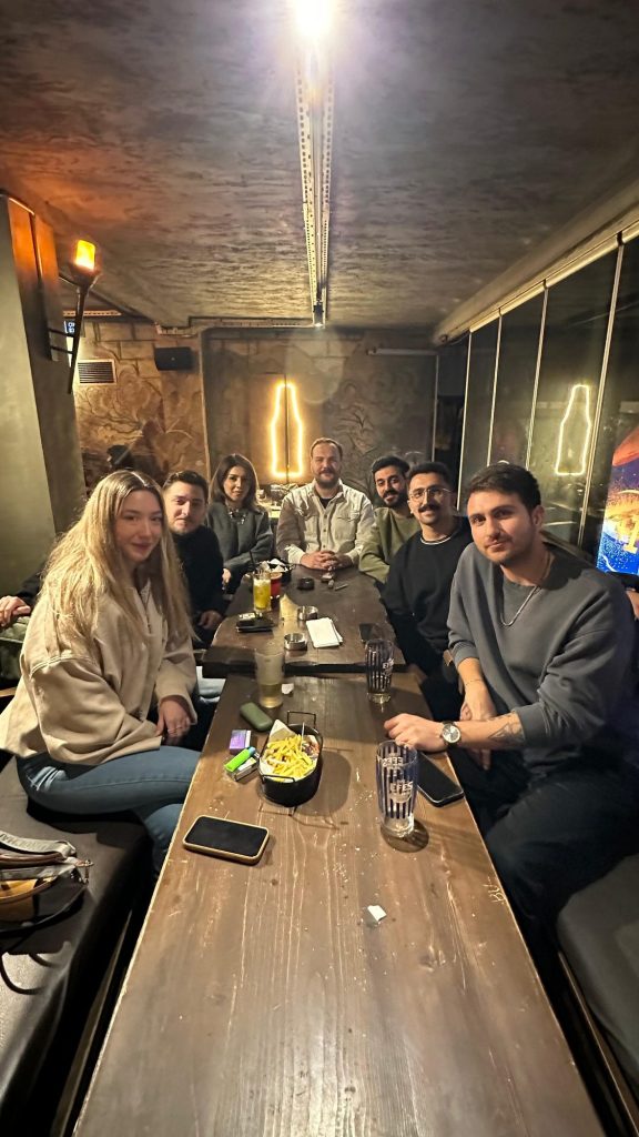 Loş ışıklı bir mekânda masada oturan grup
