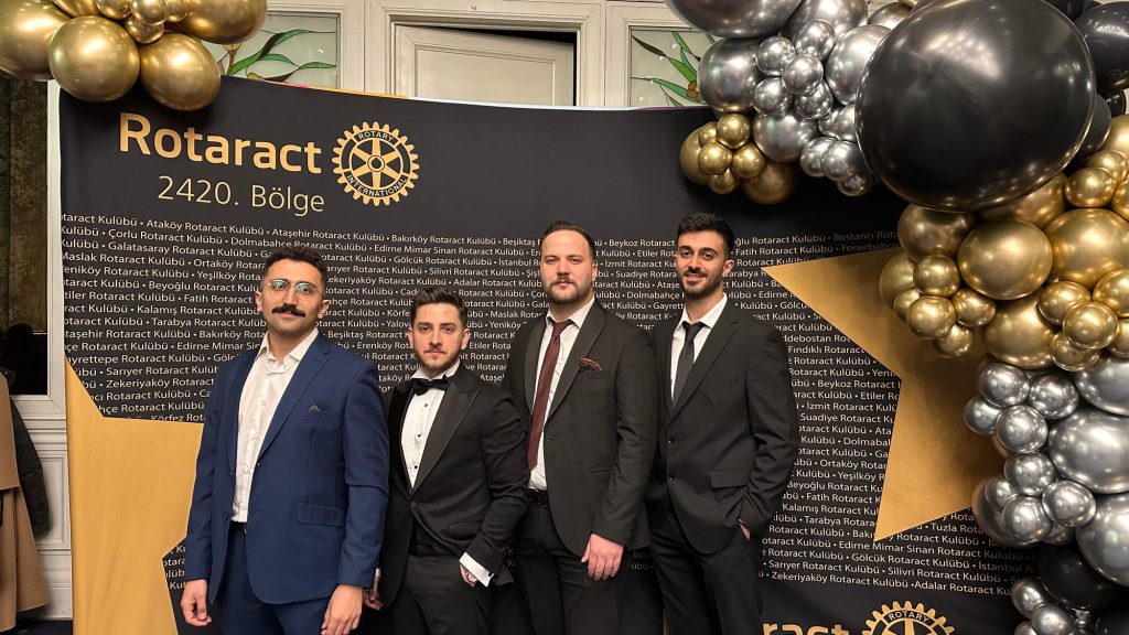 Balonlarla süslü Rotaract duvarının önünde takım elbiseli gençler
