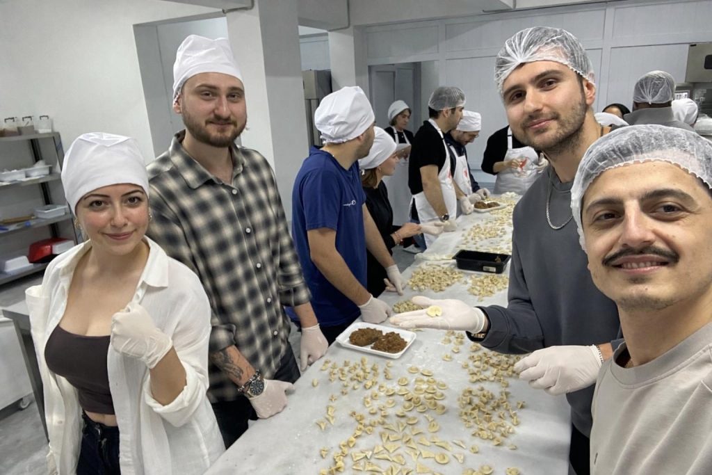 Bone ve önlük giymiş gönüllüler uzun tezgâhta mantı hazırlıyor