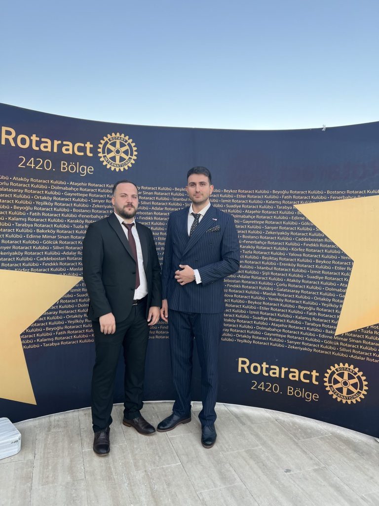 Rotaract 2420. Bölge yazılı duvarın önünde iki kulüp üyesi